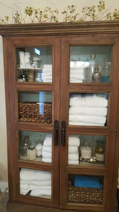 a wooden cabinet with glass doors and shelves filled with white towels