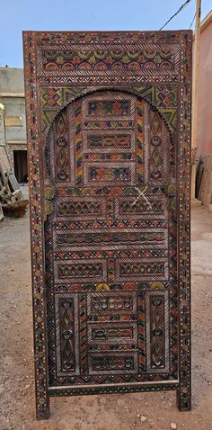 an intricately decorated wooden door in the middle of a dirt area with no people around it