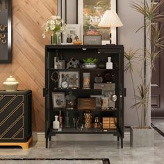 a black cabinet with pictures and other items on it next to a lamp, framed pictures and a clock