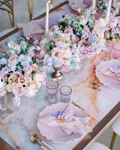 the table is set with pink and blue flowers, candles, and plates on it