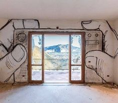 an empty room with graffiti on the wall and open doors leading to a balcony that has mountains in the distance