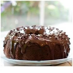 a chocolate bundt cake with frosting on a glass plate next to a window