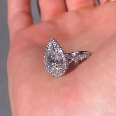 a close up of a person's hand holding a ring with a pear shaped diamond