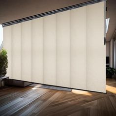 an empty room with wooden floors and white vertical blinds on the windowsill, in front of a potted plant