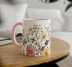 a pink and white coffee mug sitting on top of a table next to a book