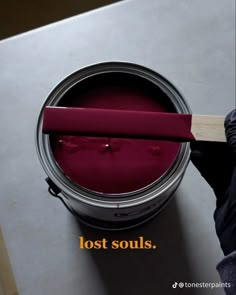 a person holding a wooden stick over a red paint can with the words lost souls on it