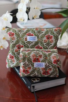 two pillows sitting on top of a wooden table next to a book and white flowers