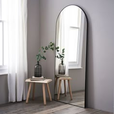 a large mirror sitting on top of a wooden floor next to a table with two vases