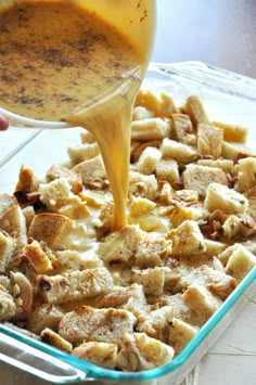 someone is pouring sauce on some food in a glass casserole dish with bread croutons