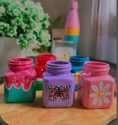 there are many different colored jars on the table and one has a butterfly painted on it