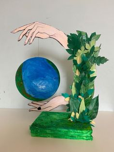 a hand reaching for a blue ball on top of a green block with greenery