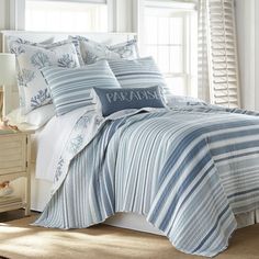 a bed with blue and white striped comforters in a bedroom next to a window