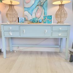 a blue table with two lamps on top and pictures on the wall in front of it