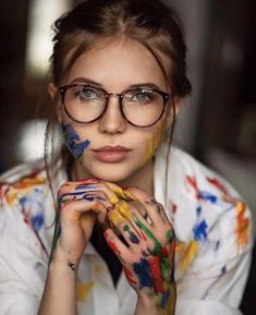 a woman with glasses and paint all over her face is posing for the camera while holding her hands to her chin