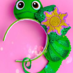 a green frog with a flower on it's head sitting in front of a pink background