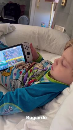 a little boy laying on top of a bed holding a nintendo wii game controller in his hand