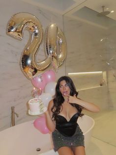 a woman posing in front of a bathtub with balloons and a cake on it