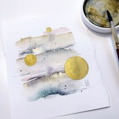 a painting with gold circles on it next to a cup of paint and a brush