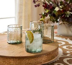 three glasses filled with water and lemon on top of a table next to a vase