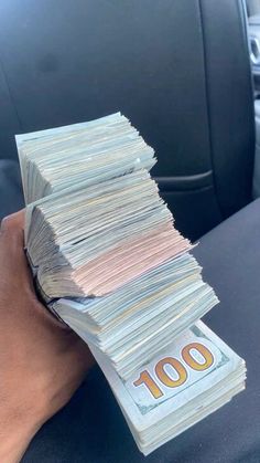 a hand holding stacks of money in the back seat of a car