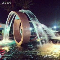 a water fountain with two circular fountains in the center and lights on behind it at night