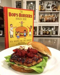 a burger sitting on top of a white plate next to a book about bob's burgers