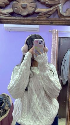 a woman taking a selfie in front of a mirror wearing a white sweater and headphones