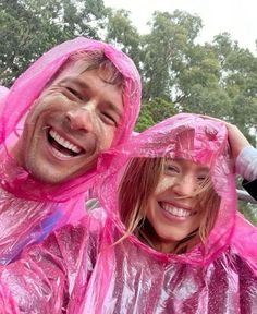 two people in pink raincoats standing next to each other with trees in the background