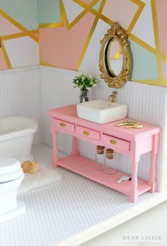 a doll house bathroom with pink vanity, sink and toilet in the background is a gold framed mirror