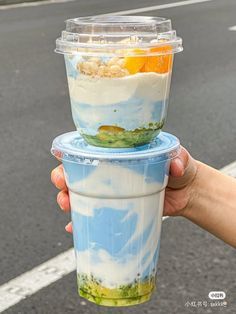 a person holding up two cups with food in them on the side of the road