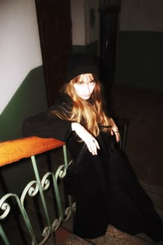 a woman sitting on top of a wooden bench next to a metal hand rail and wearing a black hat