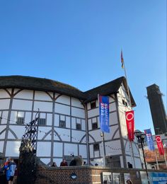 an old building with people walking around it and flags flying in the air on a sunny day