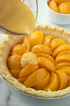 a pie crust filled with sliced peaches being drizzled with orange juice