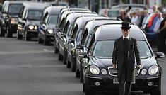 a man in a suit and top hat standing next to a line of parked cars