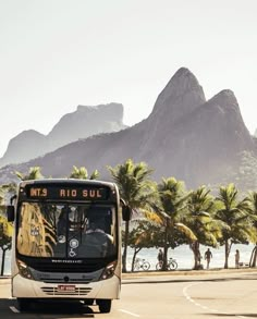 a bus is driving down the road near some palm trees and mountain in the background