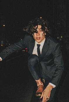 a man in a suit and tie is riding a skateboard on the street at night