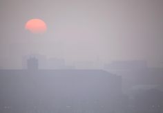 the sun is setting over some buildings in the fog