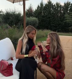 two beautiful women sitting on top of a white couch next to each other holding wine glasses