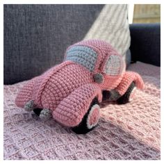 a crocheted pink car sitting on top of a couch next to a pillow