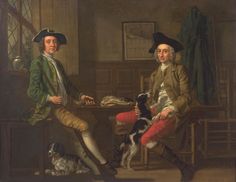 two men sitting at a table with a dog