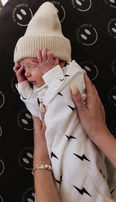 a woman holding a baby wrapped in a blanket and wearing a white knitted hat