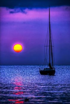 a sailboat floating in the ocean at sunset with purple and yellow colors behind it