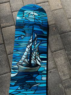 a blue skateboard with a sailboat painted on it's side sitting on the ground