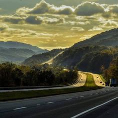 an empty highway with mountains in the background and clouds in the sky at sunset or dawn