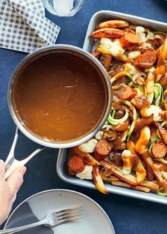 a pan filled with food next to a bowl of gravy and spoons