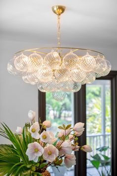 a chandelier hanging over a dining room table with flowers in the vases