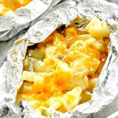 two foil wrapped food items sitting on top of a metal baking pan filled with potatoes and broccoli