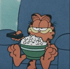 garfield the cat is eating out of a bowl with a remote control in his hand