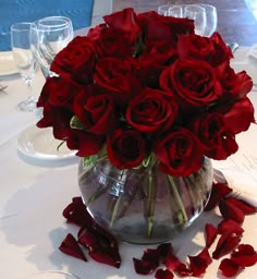 a vase filled with red roses sitting on top of a white tablecloth covered table