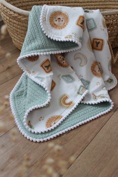 two baby blankets sitting on top of a wooden floor next to a wicker basket